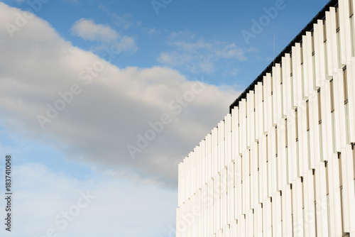 Contemporary white building facade with vertical lines under a blue sky and scattered clouds. Suitable for architecture, urban design, and modern construction themes.