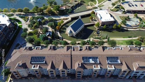 Rooftop HVAC unit on apartment complex and commercial district with canal, landscaped paths, bridges, church-like steeple, integrating cultural architecture to suburban planning, Flower Mound, TX