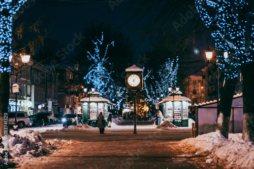 Antique clock in city square. Christmas festive decorations on street.