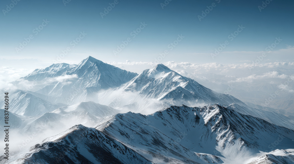 Obraz premium Majestic snow-capped mountain range under a clear blue sky, aerial view. The stunning peaks rise above the clouds, creating a breathtaking panorama of the natural world