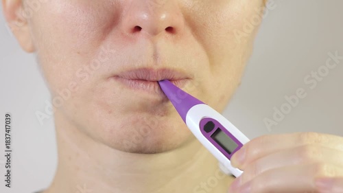 Woman is starting measure temperature at home with electronic thermometer in mouth.