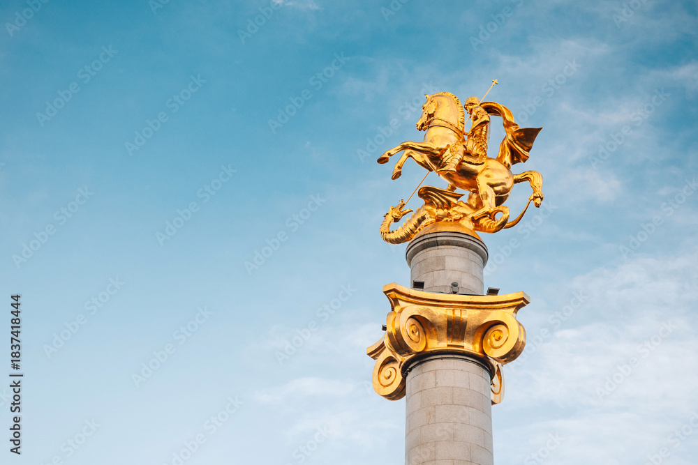 Naklejka premium 1 November 2025, Tbilisi, Georgia: Golden statue of Saint George on a tall column in the city center, representing victory and freedom