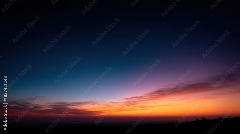 Obraz premium The sun sets over the horizon creating a blend of colors in the sky. Warm tones of orange and pink mix with cool blues showcasing a transition from day to night.