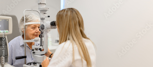 Female ophthalmologist examining senior woman's eyes with slit lamp lens in modern ophthalmology clinic