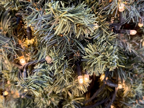 Close-up of a Christmas garland with warm glowing lights on an artificial tree, creating a cozy festive atmosphere. New year mood