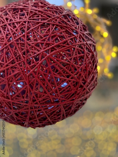 Close-up of a large red wicker Christmas ornament with glowing string lights inside. Festive holiday decor element for winter, New Year, and Christmas-themed designs