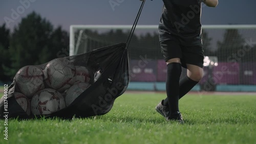 A football boy drags a bag of balls to the stadium at night