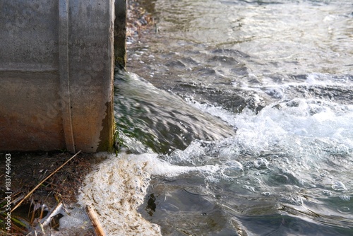 Large concrete outfall pipe, discharging water or treated effluent into river or pond with foam and debris. Wastewater from sewage treatment plants, environmental concept