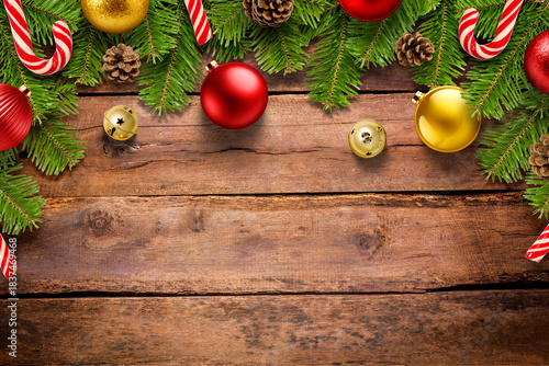 Christmas background with pine branches, jingle bells, candy cane and colorful baubles on rustic wooden table, festive holiday border with copy space. High resolution.