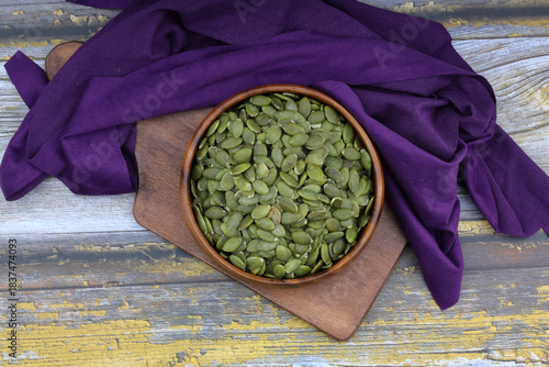 Pumpkin seeds in a wooden bowl on a wooden background