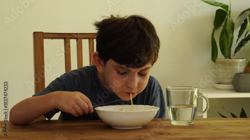 Boy eats noodles at the kitchen