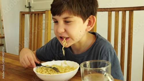 Boy eats noodles at the kitchen