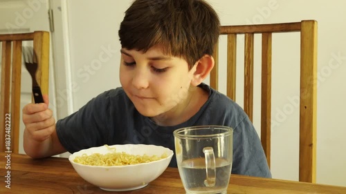 Boy eats noodles at the kitchen