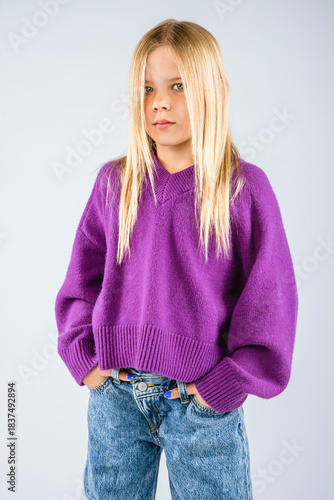 Cute blond haired young girl standing in a fuzzy purple sweater with her hands in her jean pockets