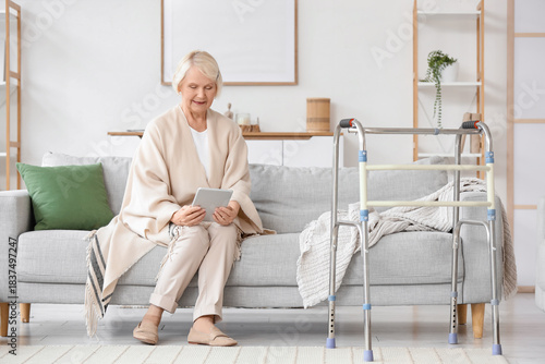 Senior woman with walker using tablet computer on sofa at home