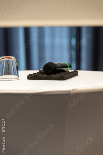 Wireless microphone and water glass on white conference table prepared for business presentation or public speaking event