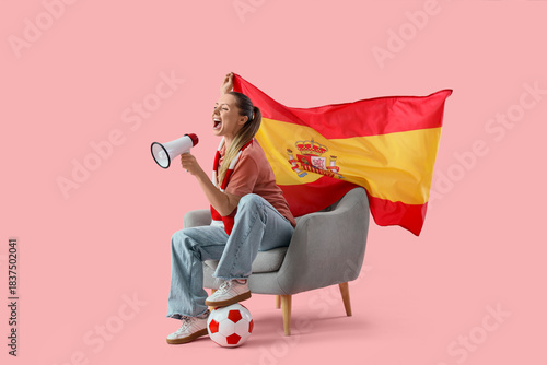 Excited female spanish football fan cheering with megaphone and flag, sitting on chair with soccer ball
