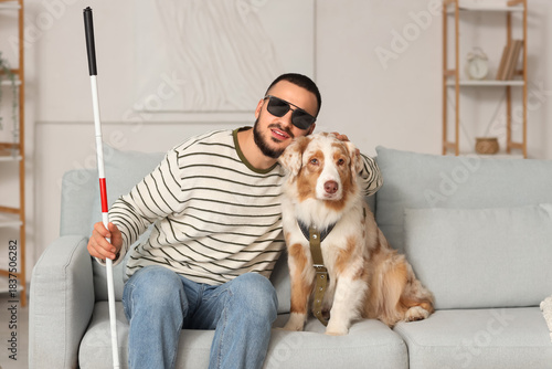 Blind young man with guide dog sitting on sofa at home