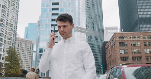 A young handsome brunette businessman makes a phone call in the city center with tall skyscrapers in the background.