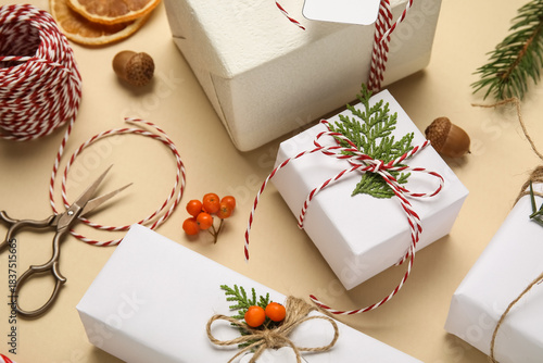 Gift boxes wrapped in eco paper with Christmas decorations, rowan berries, dried oranges and packing materials on beige background