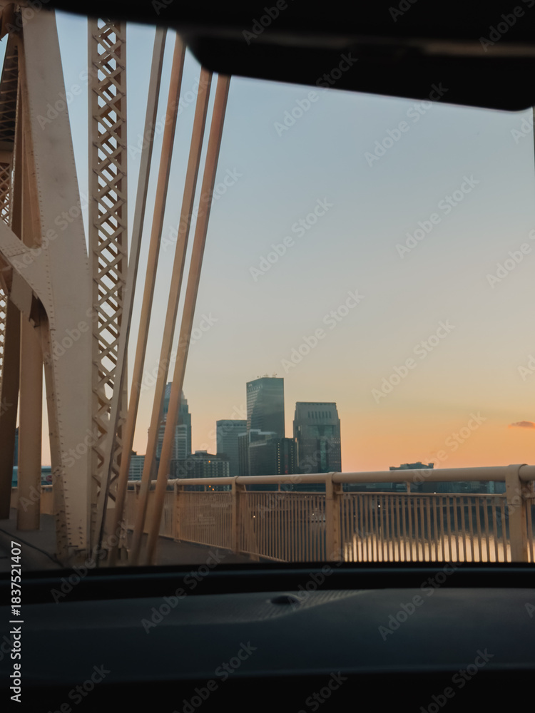 Fototapeta premium City skyline and steel bridge structure viewed through a car windshield at sunset