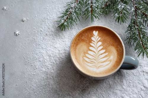 Ceramic mug holding warm beverage with latte art shaped like evergreen sits atop powdery white surface next to fir branch
