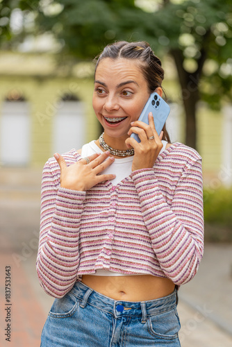 Phone call good news, gossip. Happy young woman in pleasant conversation on smartphone enjoying talking chat with friend outdoors. Girl with teeth braces walking on urban city street. Town lifestyles