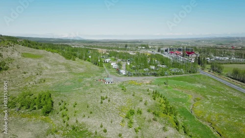 Aerial view of the campsite near the Geysir geothermal. Drone footage showing parked camper vans and the visitor center surrounded by green hills and wide open Icelandic landscapes.