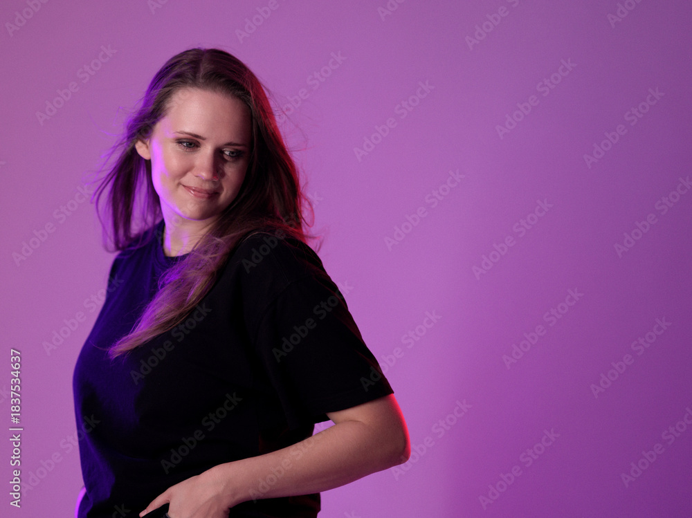 Obraz premium Studio portrait of a smiling woman with long hair wearing a black t-shirt against a purple background. This image is suitable for fashion and beauty advertising campaigns.