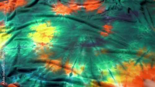 Close-up of a vibrant tie-dye t-shirt with green, yellow, and orange hues on a textured fabric surface