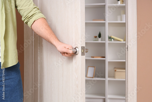 Young man closing wooden door at home, closeup