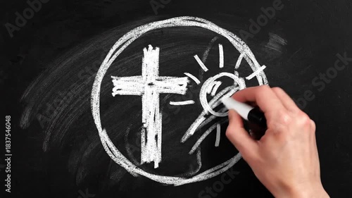 Chalk drawing a cross and sun inside a circle on a blackboard with a hand holding a marker