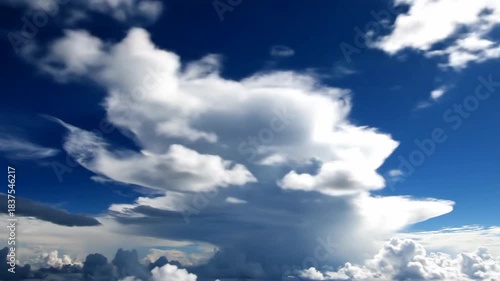 A vibrant blue sky is filled with puffy, white clouds of varying shapes and sizes, illuminated by bright sunlight