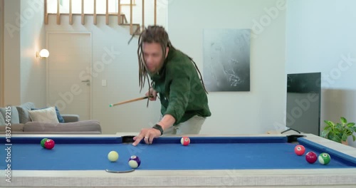 After striking ball on blue-felt pool table, man at home pumping stick realigning for next shot