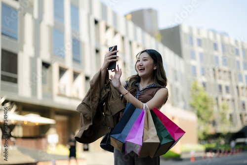 Happy young asian woman video calling while shopping in city
