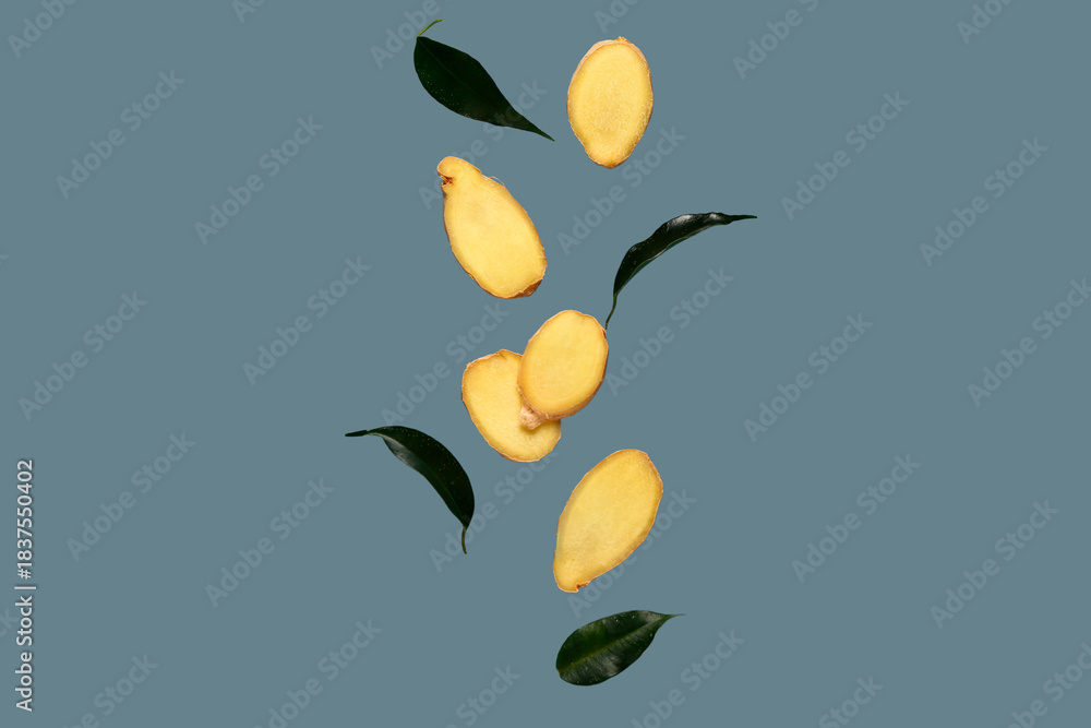 Obraz premium Flying slices of fresh ginger root and leaves on blue background