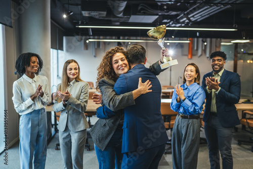 Businesswoman receiving award, embracing colleague while team applauding