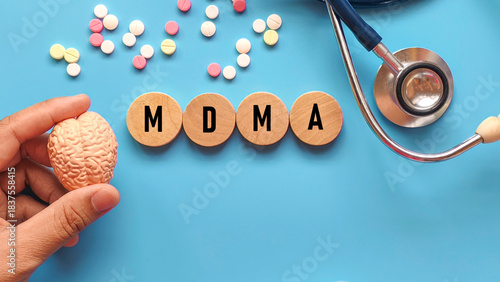 Hand Holding Brain Model Next to MDMA Acronym on Wooden Disks, Stethoscope, and Pills for Drug Research Concept
