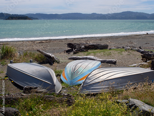 Three upturned dinghies on a beach with driftwood