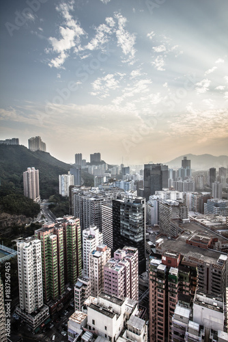 A dense cityscape with high-rise buildings and mountains under a dramatic sunset sky with glowing clouds.
