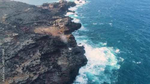 Aerial view above a blowhole in rocks on cliffs on the coast next to a sea with waves