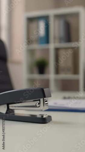 Wallpaper Mural A close-up shot of a black stapler on a desk, with an office setting in the background. The focus is on the stapler Torontodigital.ca