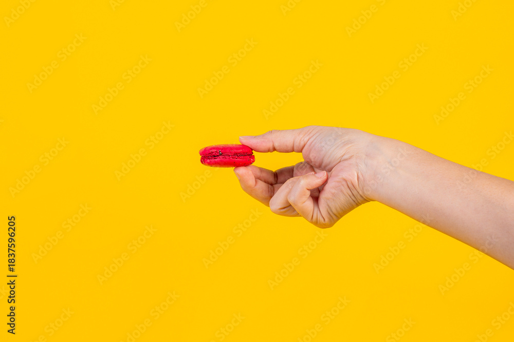 Fototapeta premium Red macarons in hand on yellow background
