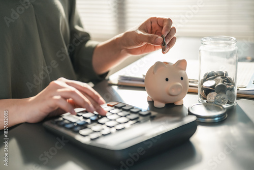 budget, planner, savings, piggybank, finance, goals, A person calculates expenses while placing coins into a piggy bank, symbolizing budgeting, savings, and personal financial planning.
