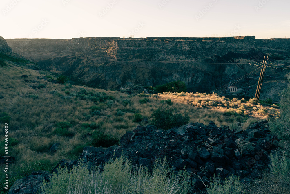Fototapeta premium Flat plains dotted with sagebrush and scrub plants extending out to the horizon under a clear blue sky, split in the middle distance by the massive Snake River Canyon just barely visible, in shadow.