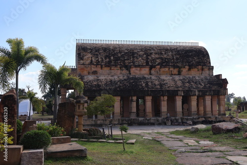 An ancient temple like structure in ruins. This building features a large entrance with multiple decorative columns, some of which are intact while others appear to be weathered or missing parts