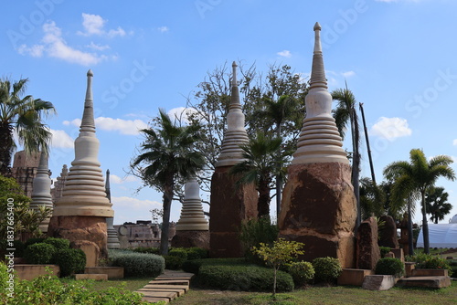 A serene setting in what appears to be a tropical location. Dominating the foreground are several Buddhist stupas, which are domed structures typically found in Buddhist temple complexes