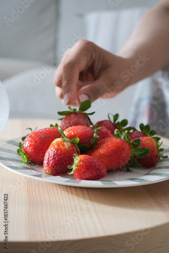 Picking strawberries from a plate on a wooden table