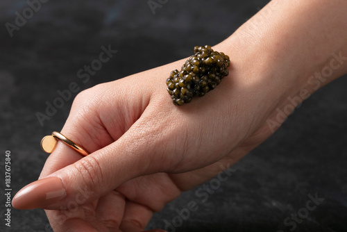 Fotografie A woman’s wrist with a small piece of caviar - black background.