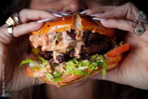 A young woman taking a large bite out of a hamburger On a dark background.